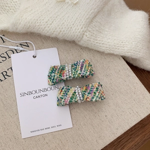 Detailed view of tweed bow hair clips with faux pearls on a beige display board