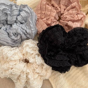 Close-up of four lace scrunchies in pastel colors on a textured knit background