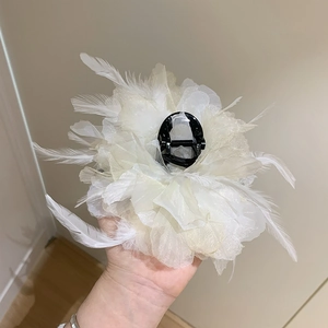 Detail of white feather and petal floral hair claw clip shown from a side perspective
