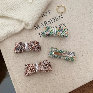 Detailed macro view of tweed bow hair clips with faux pearls on a beige fabric background