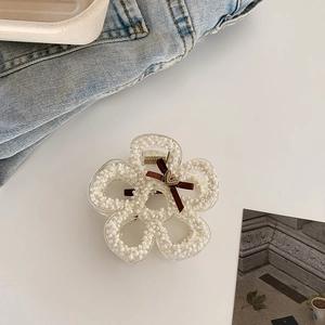 Close-up of pearl flower hair claw with brown bow and golden heart charm on white surface
