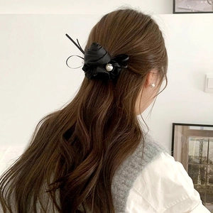 Elegant black satin rose hair clip with white pearl detail on model hair