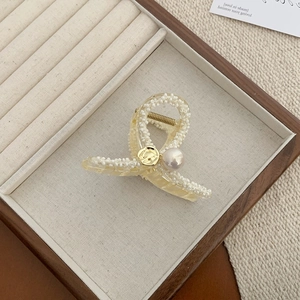 Elegant amber resin hair claw with white beads and pearl on a wooden jewelry tray