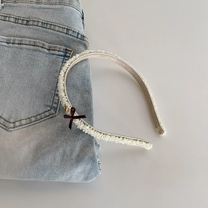 Detail of white textured headband featuring a brown silk bow and small gold metal charm