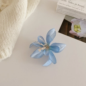 Détail d'une pince à cheveux magnolia en soie bleu clair sur un fond en maille blanche