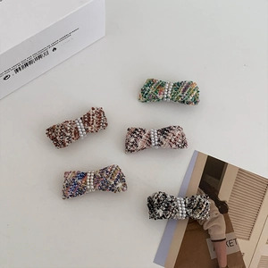 Detail of tweed bow hair clips with pearls in five colors on a white minimalist background