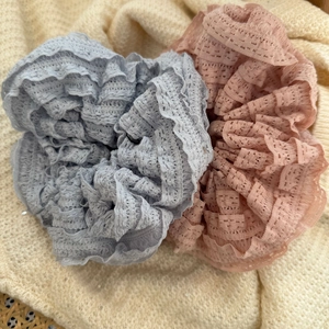 Detailed view of layered lace scrunchies in pink and grey colors on knit background