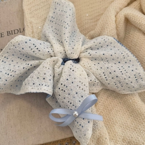 Gros plan d'un chouchou en dentelle blanche à pois bleus avec détail de perle centrale
