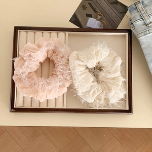 Dettaglio di elastici scrunchie oversize rosa e crema con bordi piumati su vassoio