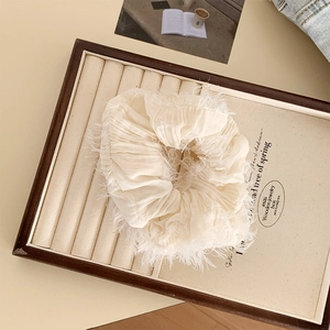Dettaglio di scrunchie beige crema con bordi sfrangiati su un vassoio per gioielli