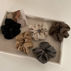 Detail of five earth-toned satin hair scrunchies displayed in a beige fabric tray