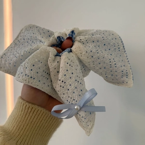 Détail d'un chouchou à nœud en dentelle florale avec tissu à carreaux bleu et perle