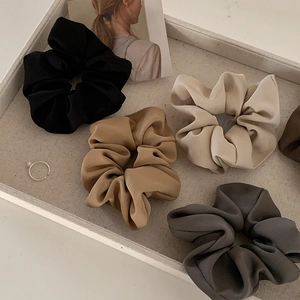 Detailed close-up of premium satin scrunchies in neutral colors on a display tray
