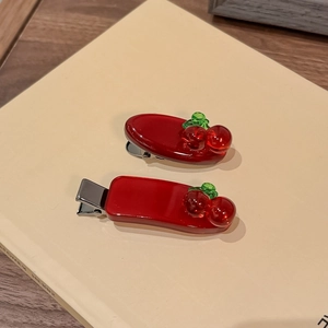 Zweiteiliges Set rote Kirsch-Haarspangen aus Harz mit Entenschnabel-Clip auf einem Buch