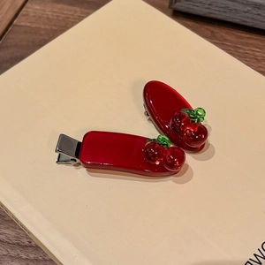 Paar rote Kirsch-Haarspangen mit grünen Blättern auf Buch für einen Vintage-Ästhetik-Stil