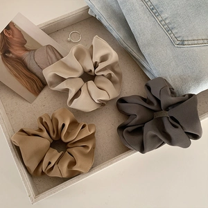 Three premium satin scrunchies in cream and brown tones on a minimalist textured tray