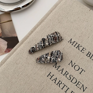 Close-up of elegant tweed fabric hair clips with colorful knit texture on a canvas book