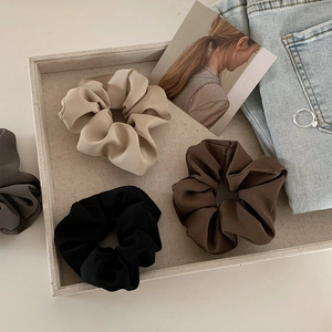 Close-up of silky satin scrunchies in neutral earth tones with pleated texture details