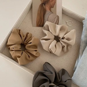 Detailed view of satin hair scrunchies in caramel, beige, and grey on a fabric tray