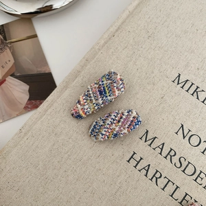 Close-up of two multi-colored tweed fabric snap hair clips on a textured book cover