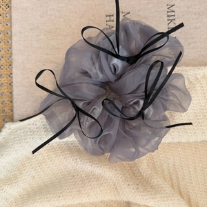 Détail d'un chouchou en tulle gris orné de cinq nœuds en ruban noir sur un tissu en maille douce