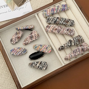 Close-up of colorful tweed woven hair clips set on a wooden display tray with metal backings