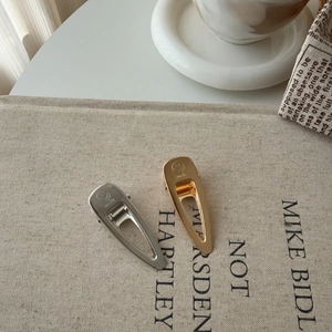 Polished metal teardrop hair clips with smile engraving on textured book background
