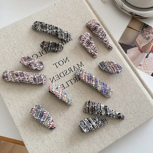 Elegant tweed fabric hair clips in assorted patterns on a beige textured book background