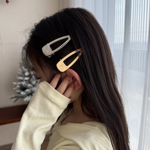 Golden hollow hair clip with smile engraving worn by a model in a cozy indoor setting