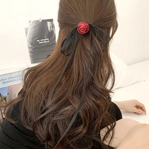Detailed back view of a burgundy fabric rose and long black ribbons tied in long wavy hair