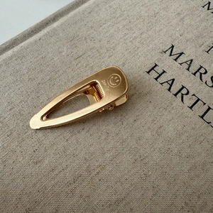 Close-up of golden teardrop metal hair clip with Smile engraving on matte finish fabric