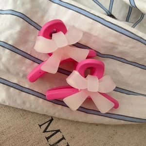 Détail de petites pinces à cheveux rose vif avec des nœuds blancs mats sur tissu rayé