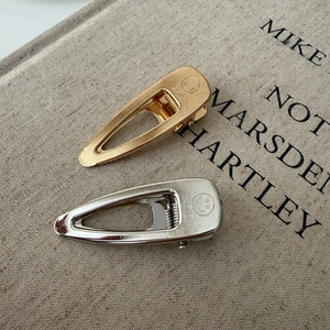 Detail of gold and silver metallic smile hair clips on a minimalist beige canvas background