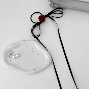 Close-up of a burgundy rose hair scrunchie with black ribbon and pearl drop earrings on a tray
