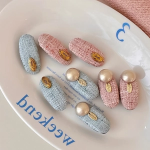 Detailed close-up of tweed hair clips with faux pearls and gold charms on white ceramic tray