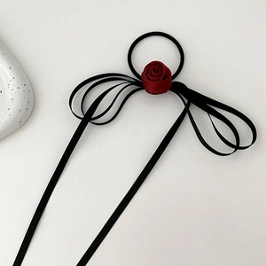 Detail of a dark red velvet rose hair tie with long black silk ribbons on a grey surface