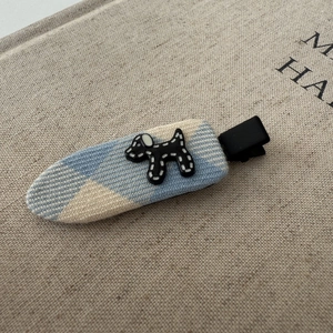 Detail of blue woven fabric hair clip with a cute black and white dog mascot ornament
