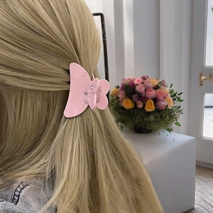 Vue détaillée d'une pince à cheveux papillon rose en acétate sur des cheveux blonds dorés