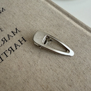Silver metal teardrop hair clip with smile engraving on minimalist beige linen background