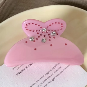 Détail d'une pince à cheveux nœud rose en acétate ornée de strass brillants élégants