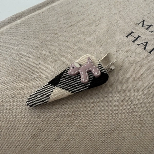 Detailed shot of a polka dot puppy resin charm on a black and white tweed hair clip