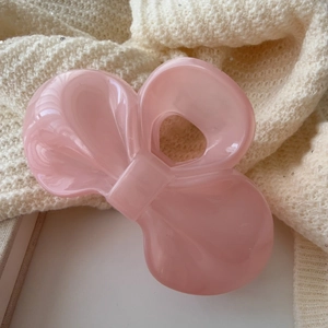 Close-up of a light pink bow hair claw clip with pearlescent texture on a soft background