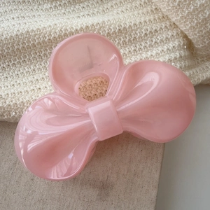 Detailed view of a pink bow-shaped hair claw clip with a glossy translucent finish
