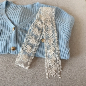 Detailed view of delicate white floral lace embroidery on light blue knitted cardigan