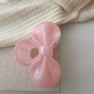 Close-up of pink ribbon hair claw clip on beige knitted fabric with soft warm tones