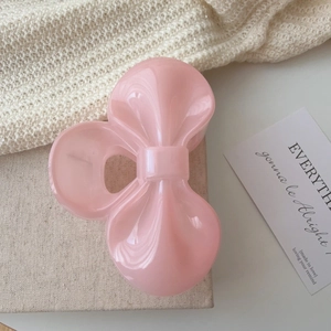 Close-up of a pink bow hair claw clip on a soft aesthetic fabric background