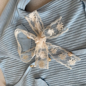 Detail of light blue knit fabric with cream lace bow and decorative golden buttons