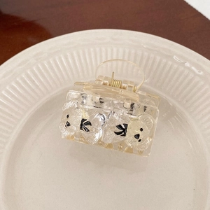 Detail view of champagne acrylic bear hair claw clip with black bows on white plate
