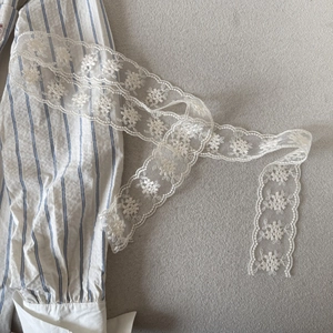 Macro detail of delicate white floral lace ribbon with embroidery on a striped shirt