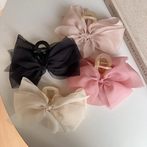 Detail of large chiffon bow hair claws in pink, beige, and black on a white table